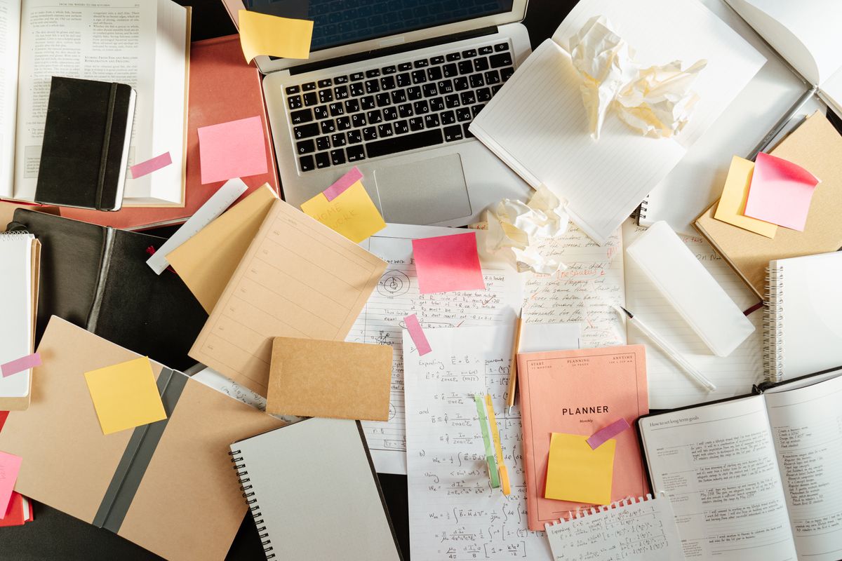 A student's desk buried under notebooks, worksheets, sticky notes and crumpled paper